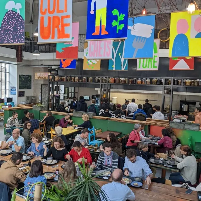 La salle de La Fabuleuse Cantine à Saint-Étienne à l’heure du déjeuner : grandes tablées, file au comptoir sous les affiches colorées suspendues.